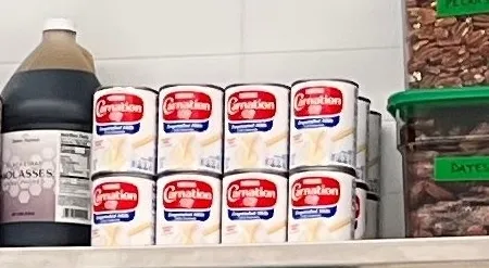 Two stacked rows of four Carnation evaporated milk cans on the shelf, next to a jug of molasses