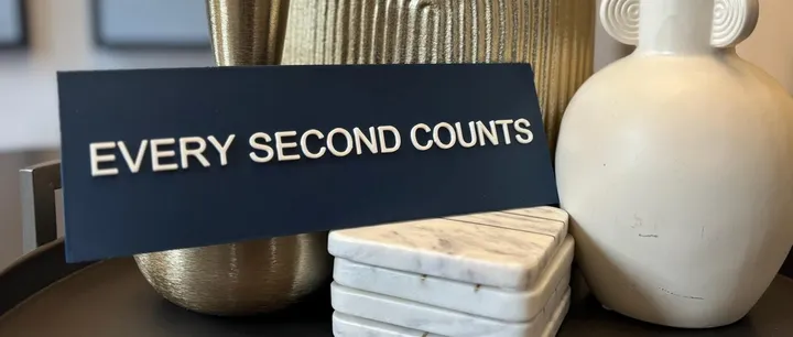 An Etsy version of the sign: a black plaque with raised white letters, styled on a shelf with vases and coasters