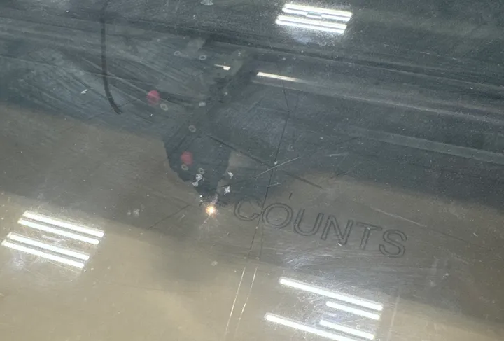 A laser cutter engraving “COUNTS” into a sheet of acrylic