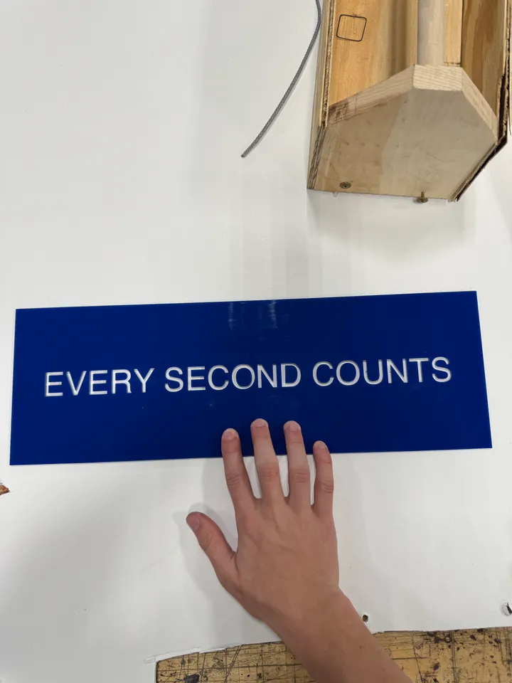 A finished navy panel with the letters cut out, laid on white paper with a hand for scale