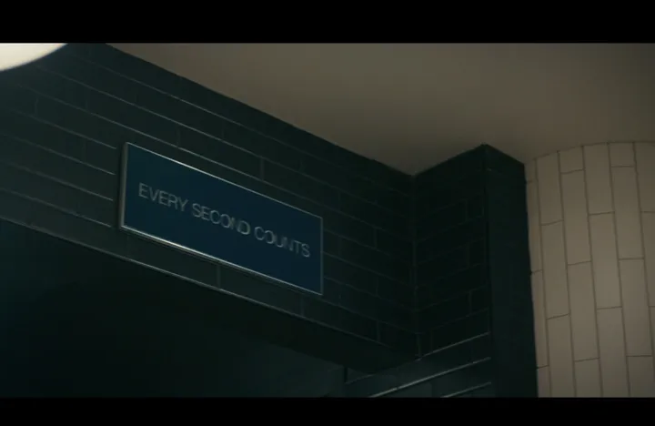 Season 2 still: the sign mounted high on a dark tiled wall in a dim kitchen in Copenhagen