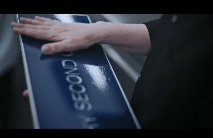 Season 3 still: a hand resting on the sign, showing its rippled, glossy surface and recessed letters